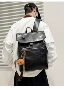Detail of black faux leather backpack featuring a plush bear charm and side pockets