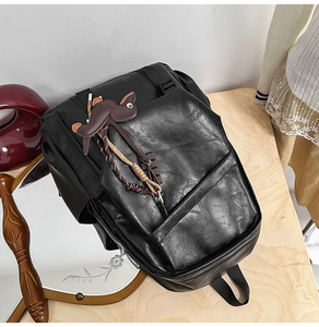 Detail of black leather backpack texture with a cute brown cartoon mouse charm accessory