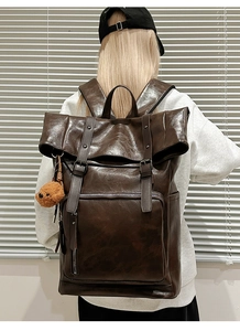 Detail of dark brown leather backpack featuring a roll-top closure and plush bear pendant