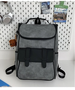 Detail view of a gray and black PU leather backpack with a plush bear charm on a desk