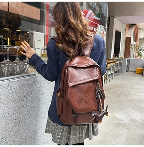 Detail of vintage brown leather backpack with puppy charm in a cozy cafe setting
