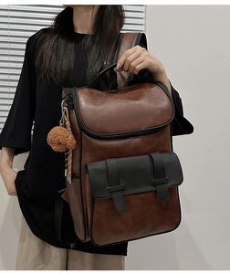 Detail view of a vintage PU leather backpack featuring magnetic straps and plush bear charm