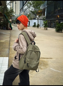 Detail view of the khaki grid pattern nylon backpack worn by a model on a city street