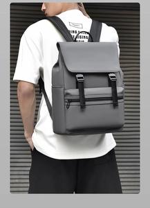 Rear view of a man wearing a dark grey streetwear backpack with flap cover and buckle straps