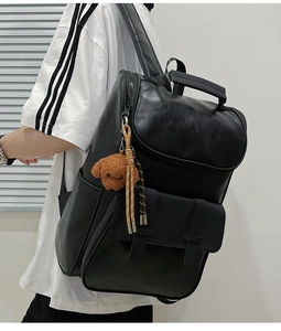 Detail of black PU leather backpack showing side pocket and bear keychain accessory