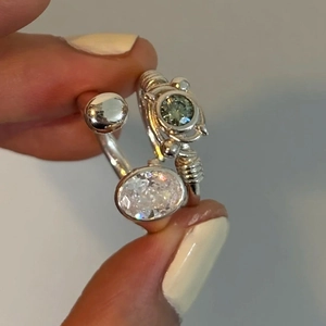 Détail de bagues argentées superposées avec zircon ovale et pierre gemme verte