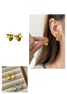 Detail view of hollow bow and heart earrings in gold and silver showing on-ear style