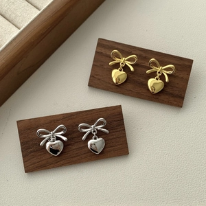 Elegant gold and silver bow heart earrings displayed on a premium wood texture stand