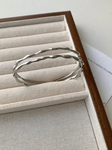 Detailed view of silver wave-patterned open bangle with polished metallic finish