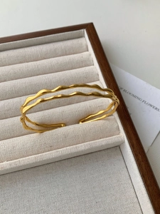 Close-up of golden double-layered wavy cuff bracelet on beige velvet jewelry display