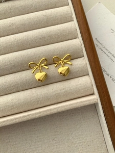 Detail of golden bow and heart earrings displayed on a premium beige velvet jewelry tray
