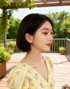 Detail of elegant gold bow earrings with a red pearl drop worn in a sunny outdoor setting