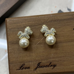 Elegant gold puppy pearl earrings with sparkling cubic zirconia on a rustic wooden stand