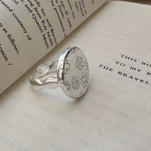 Adjustable floral disc silver ring with wavy textured band on an open book background