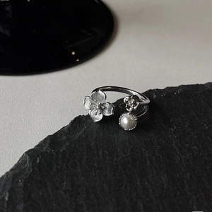 Macro detail of silver floral ring with matte petal texture and glossy faux pearl inlay