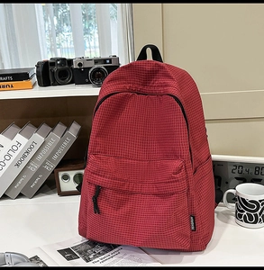 Detail of red checkered nylon backpack with brand tag in a cozy lifestyle setting
