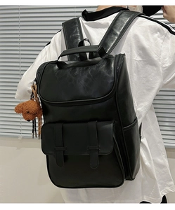 Side view of black PU leather backpack with decorative buckles and brown bear plush charm