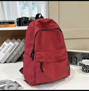 Detail of red checkered nylon backpack featuring front zip pockets and side brand label