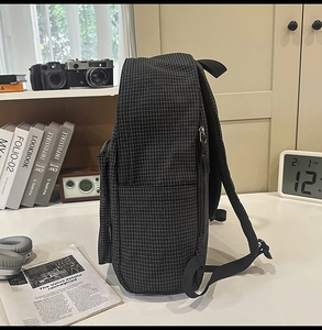 Detail view of plaid nylon backpack featuring a side zipper pocket and mesh strap