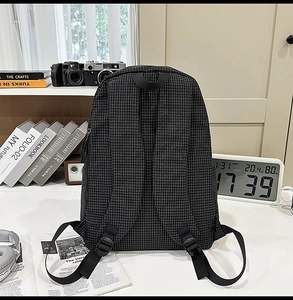 Detail of black checkered nylon backpack showing adjustable straps and durable back padding