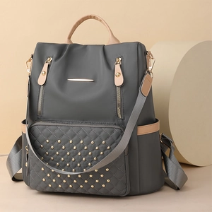 Detail eines grauen Stepprucksacks mit goldenen Nieten und hellbraunen Ledergriff-Akzenten