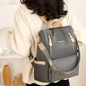 Detail eines grauen gesteppten Rucksacks mit goldenen Nieten und Ledergriffen