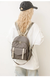 Détail d'un sac à dos matelassé taupe avec fermetures dorées porté par un modèle