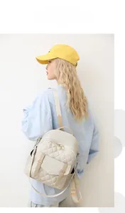 Gros plan d'un sac à dos matelassé beige avec surpiqûres en losange et détails zippés en métal