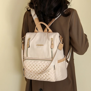 Detail eines beigen Stepprucksacks mit goldenen Nieten, getragen auf braunem Mantel