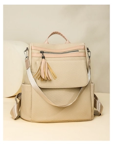 Detail of beige woven texture backpack featuring a decorative tassel and front zipper pocket