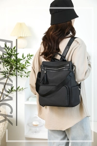 Detail of black textured backpack with tassel zipper and spacious front pocket shown on model