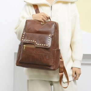 Detail view of large brown PU leather backpack with rivet accents and zipper pockets