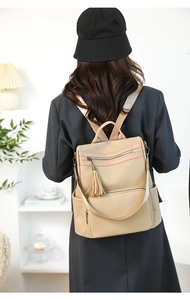 Beige vintage backpack with tassel detail shown on model in a stylish indoor setting