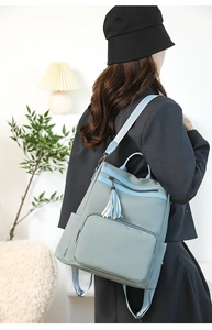 Detail view of woven grey backpack featuring light blue straps and bi-color fringe tassel