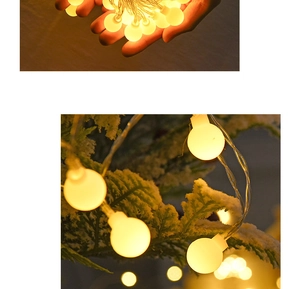 Close-up of warm white LED frosted ball string lights on hands and snowy pine branches