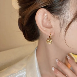 Détail d'une boucle d'oreille cheval à bascule dorée portée par un mannequin sous lumière