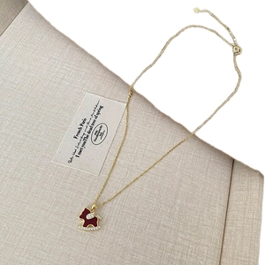 Collier cheval à bascule doré avec pendentif en zircon rouge sur fond beige épuré