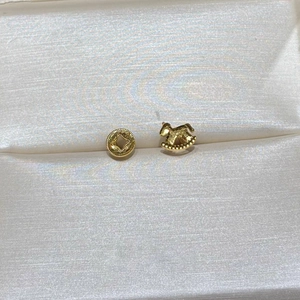 Detail of gold rocking horse stud earring with hollow round coin design on white silk