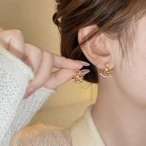 Golden carousel horse earrings with red enamel and pavé crystals worn by a model