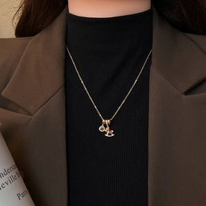 Golden necklace with rocking horse and ring pendants worn on dark turtleneck and brown blazer