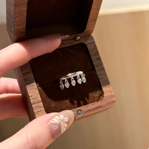 Close-up of silver tassel ring with teardrop gemstones in a premium wooden jewelry box