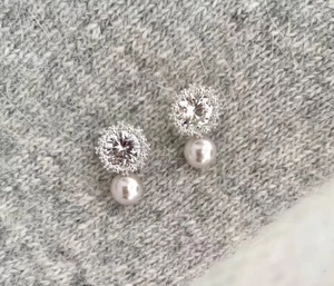 Detail shot of snowflake pearl earrings with silver base and zircon on grey knit fabric