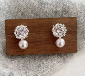 Close-up of pearl and zircon stud earrings featuring a snowflake design on a wooden display