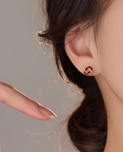 Vue détaillée de boucles d'oreilles nœud en émail rouge et doré sur l'oreille