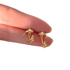 Minimalist golden dolphin stud earrings with double-sided hanging design held by hand