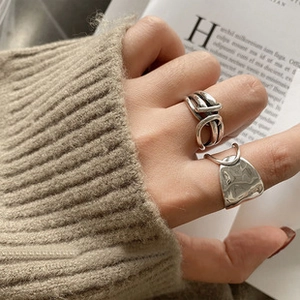 Close-up of retro silver rings featuring braided knot and hammered textures on a model