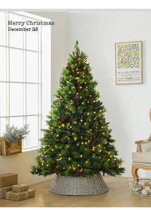 Close-up of artificial Christmas tree with LED lights, red berries, cones and woven tree skirt