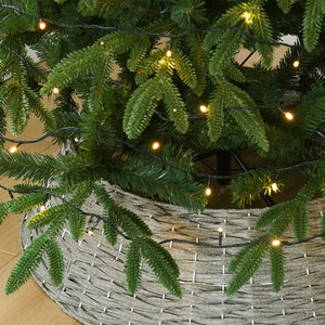 Sapin de Noël vert avec lumières et jupe de sapin en saule tressé gris décorative
