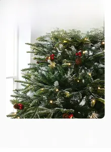 Detail of pine cones, red berries and warm LED lights on a snowy Christmas tree