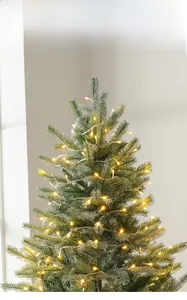 Détail du sapin de Noël artificiel luxuriant avec pointes enneigées et guirlandes LED chaudes